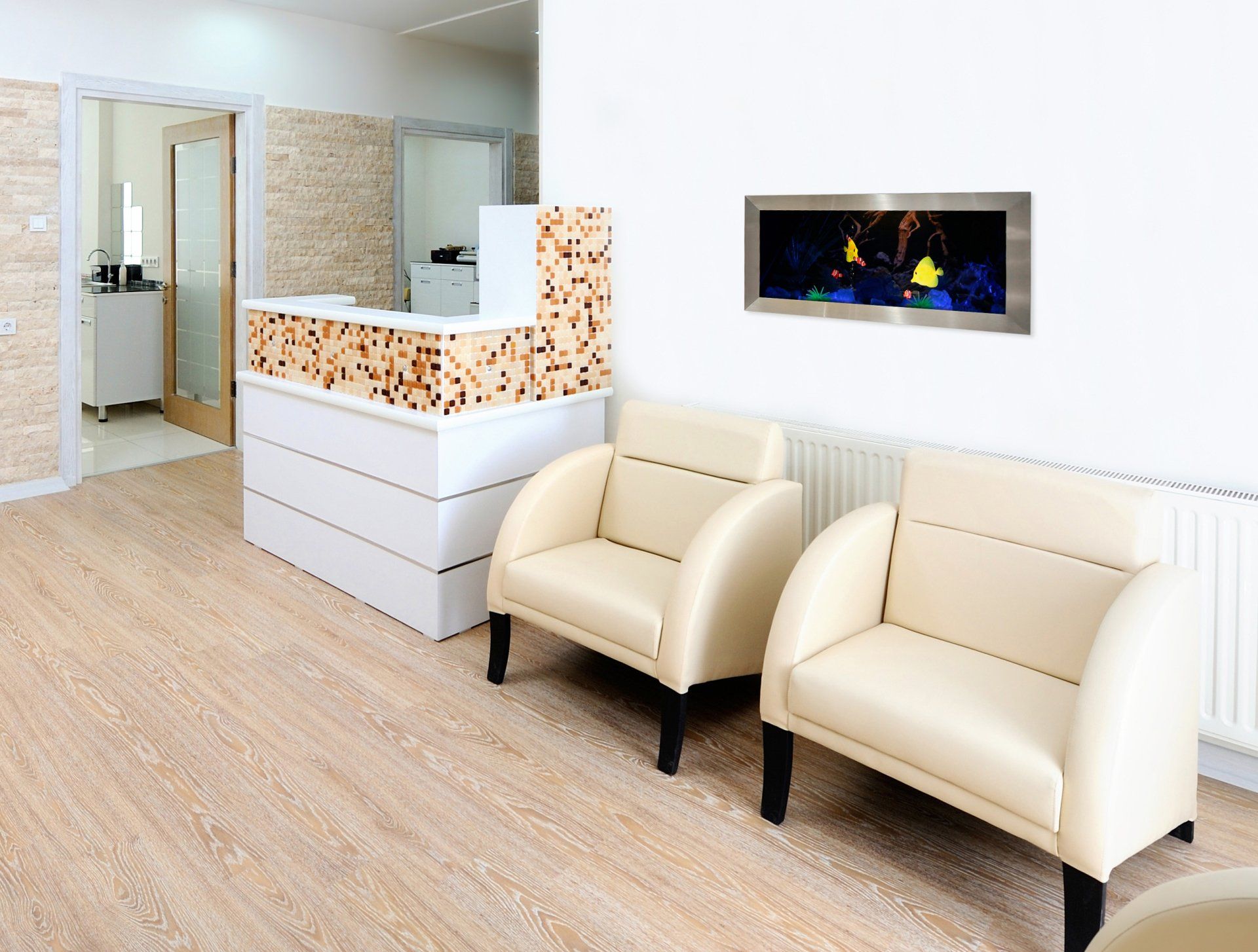 Reception area with white chairs, wooden desk, and fish tank on the wall.