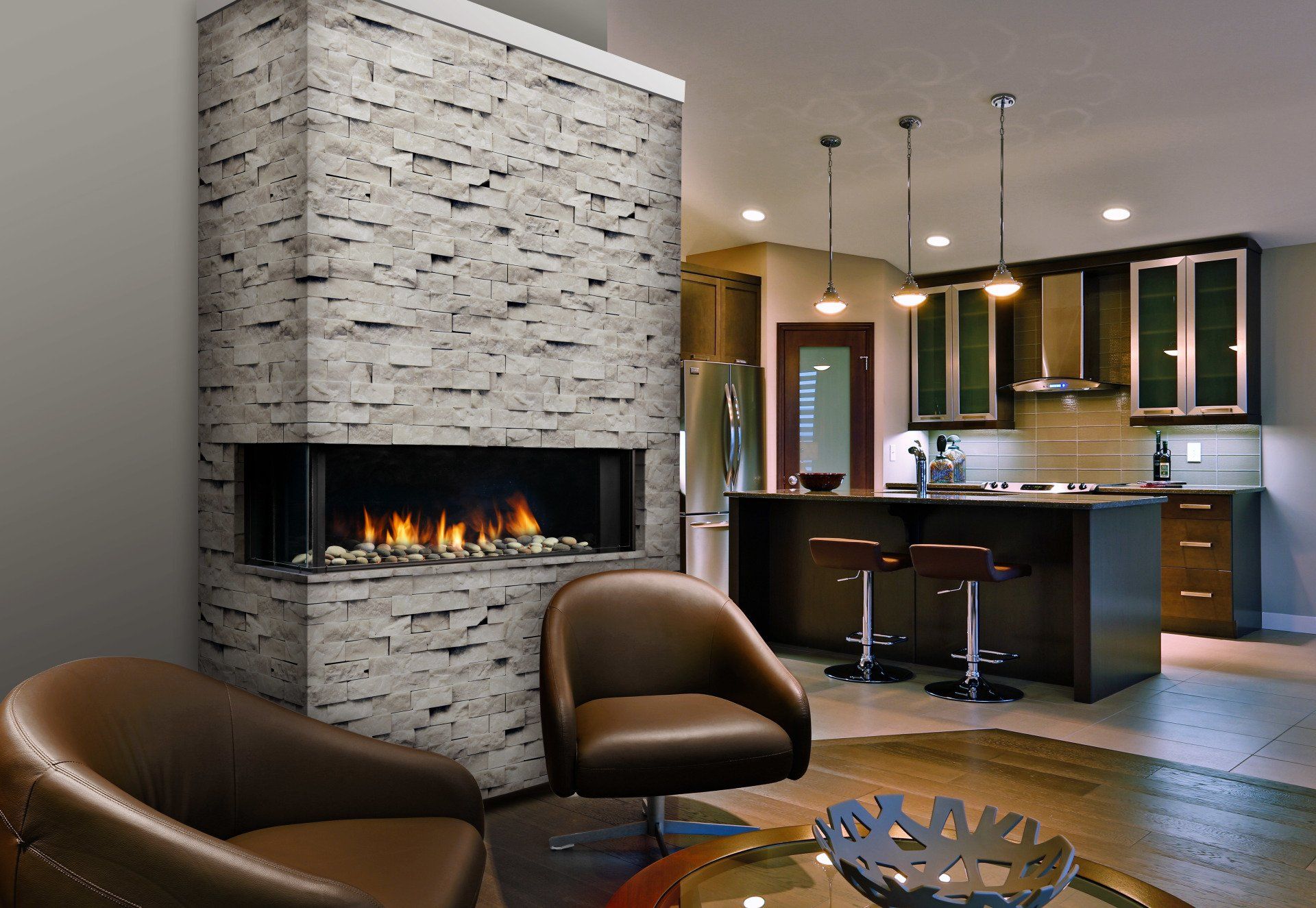 Modern living room with a stone fireplace, open to a kitchen with dark cabinetry and island seating.