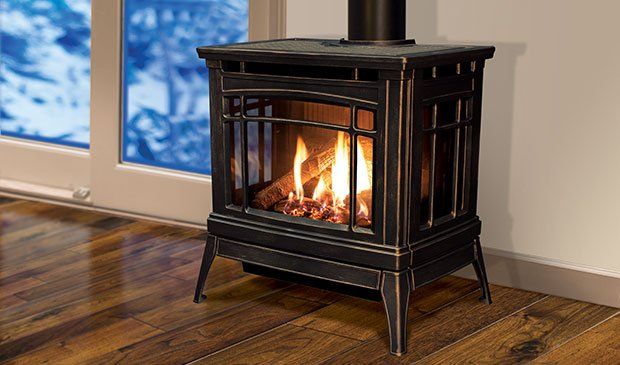 Black gas fireplace with flames, inside a room with a window, on a hardwood floor.