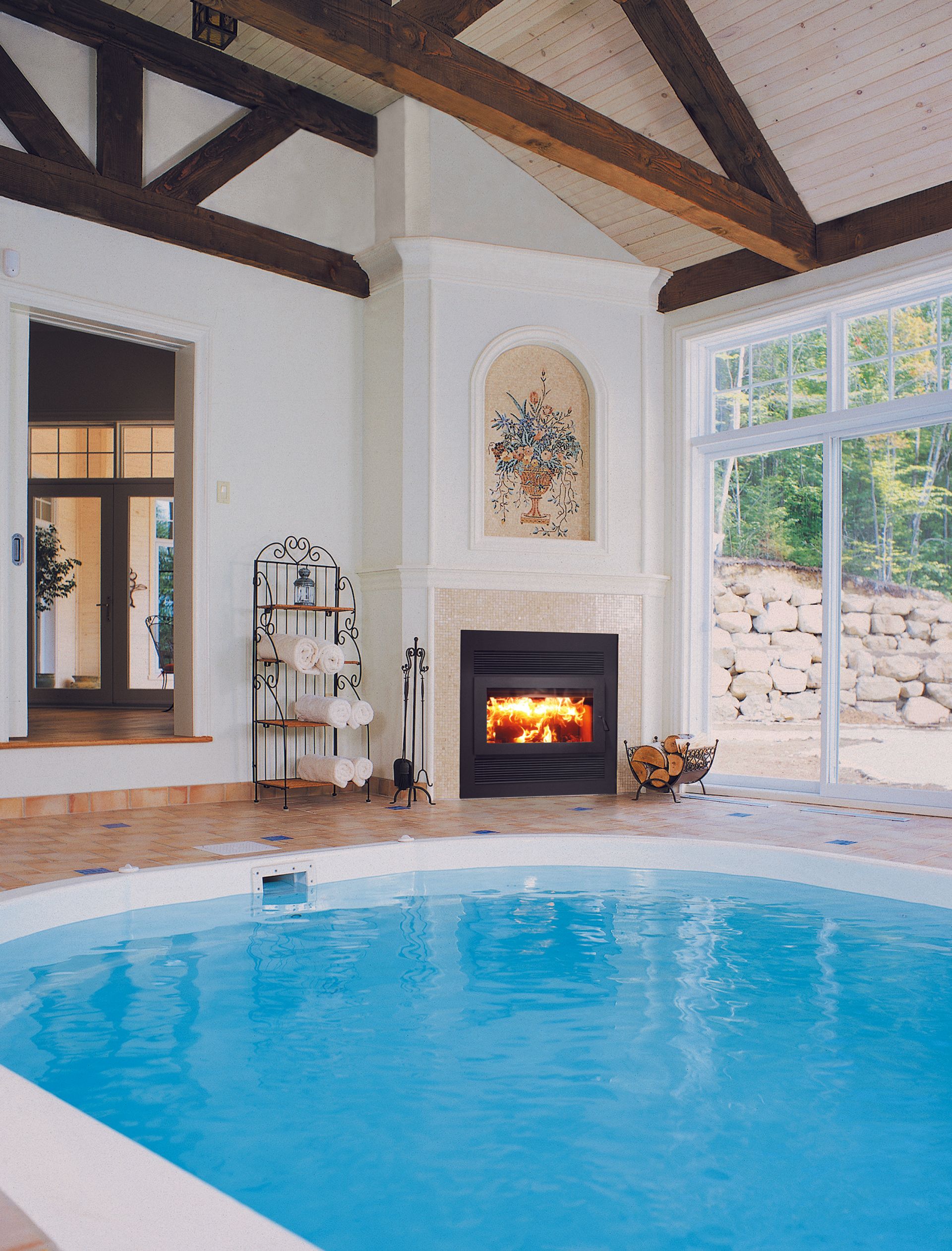 Indoor pool with fireplace, large windows, and exposed wooden beams.