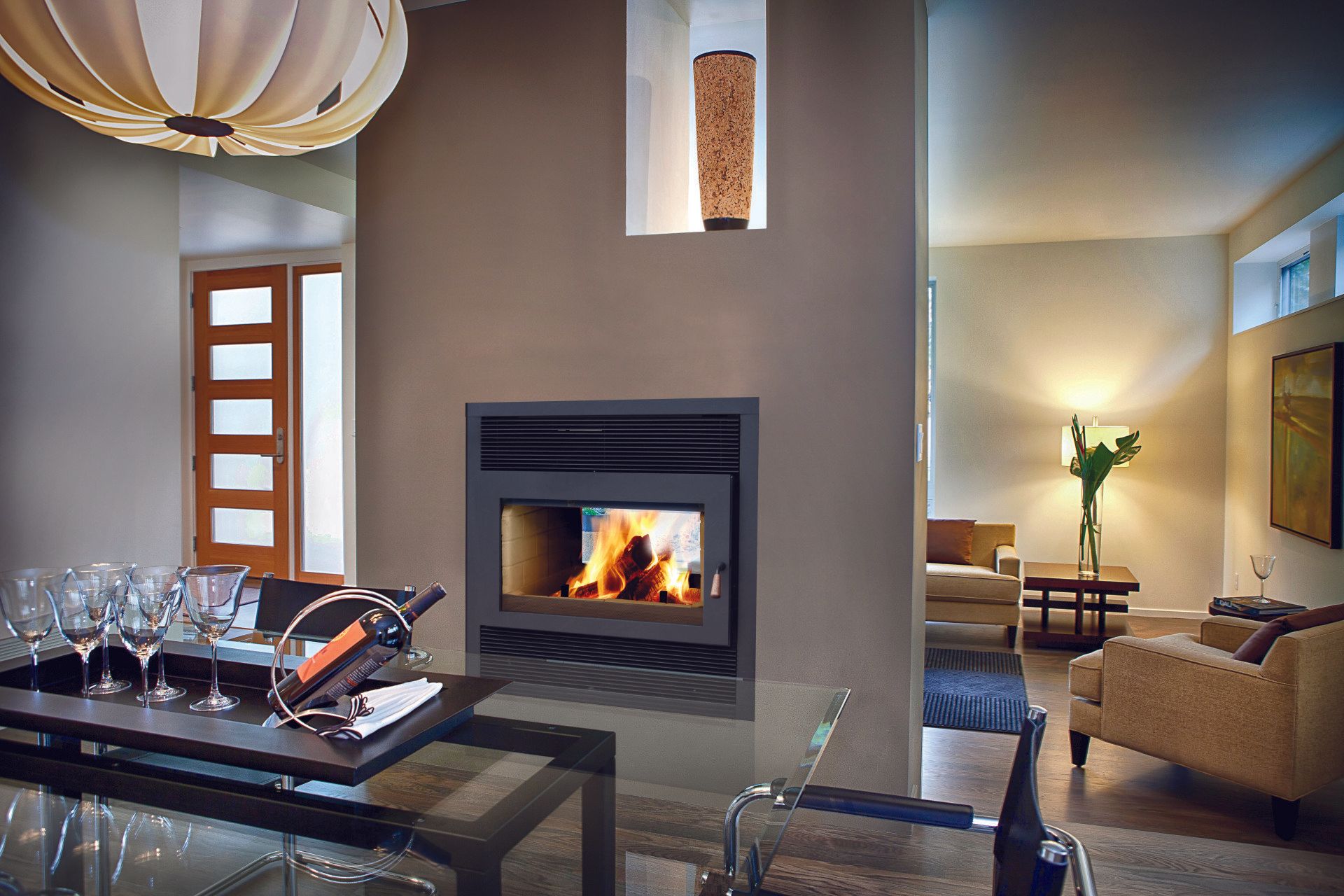 Cozy fireplace in a modern dining room setting, with glass table, wine glasses, and a doorway leading to a living area.