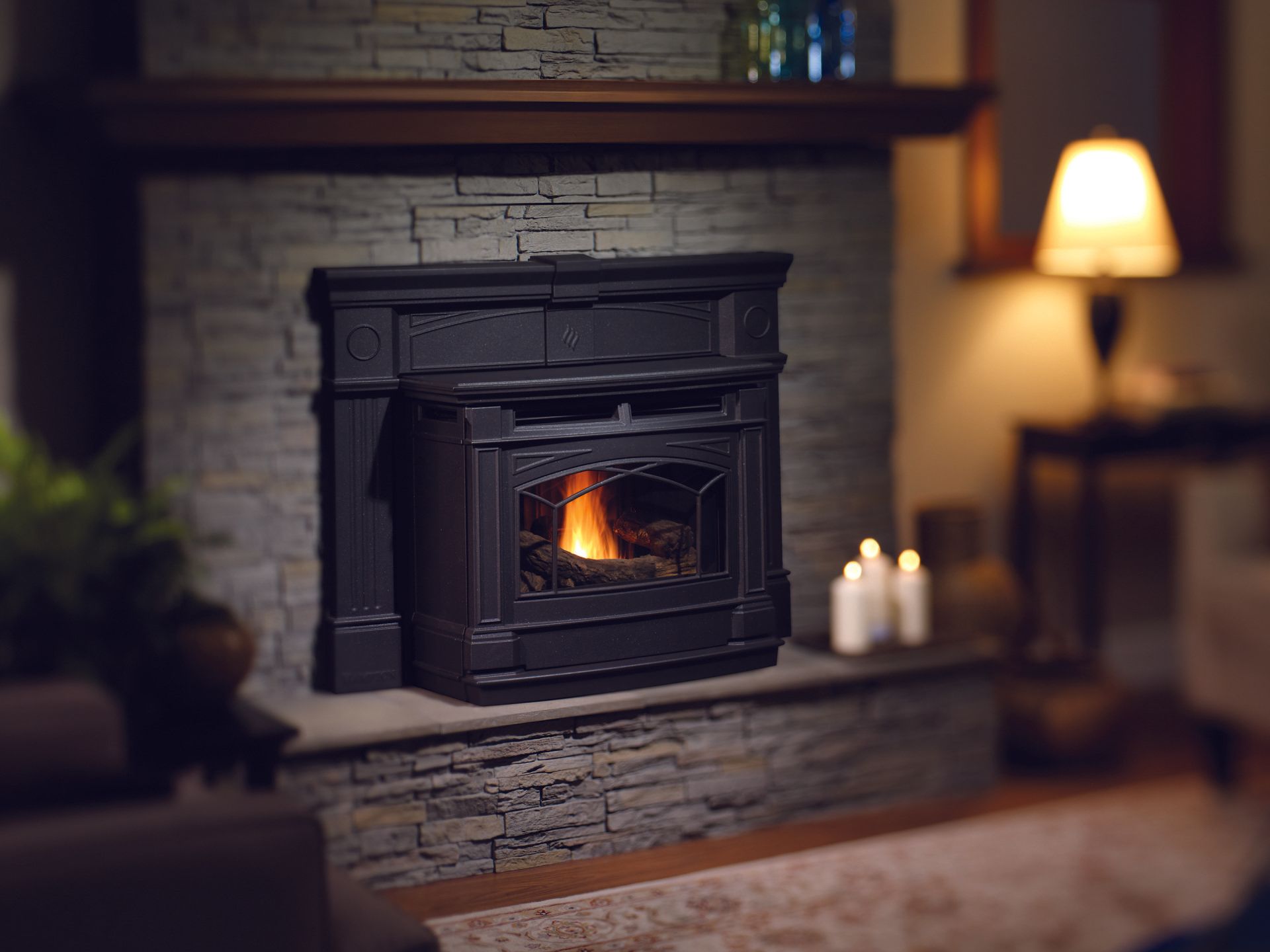 Black fireplace with a lit flame, set in a stone surround, and topped with a dark wood mantel.