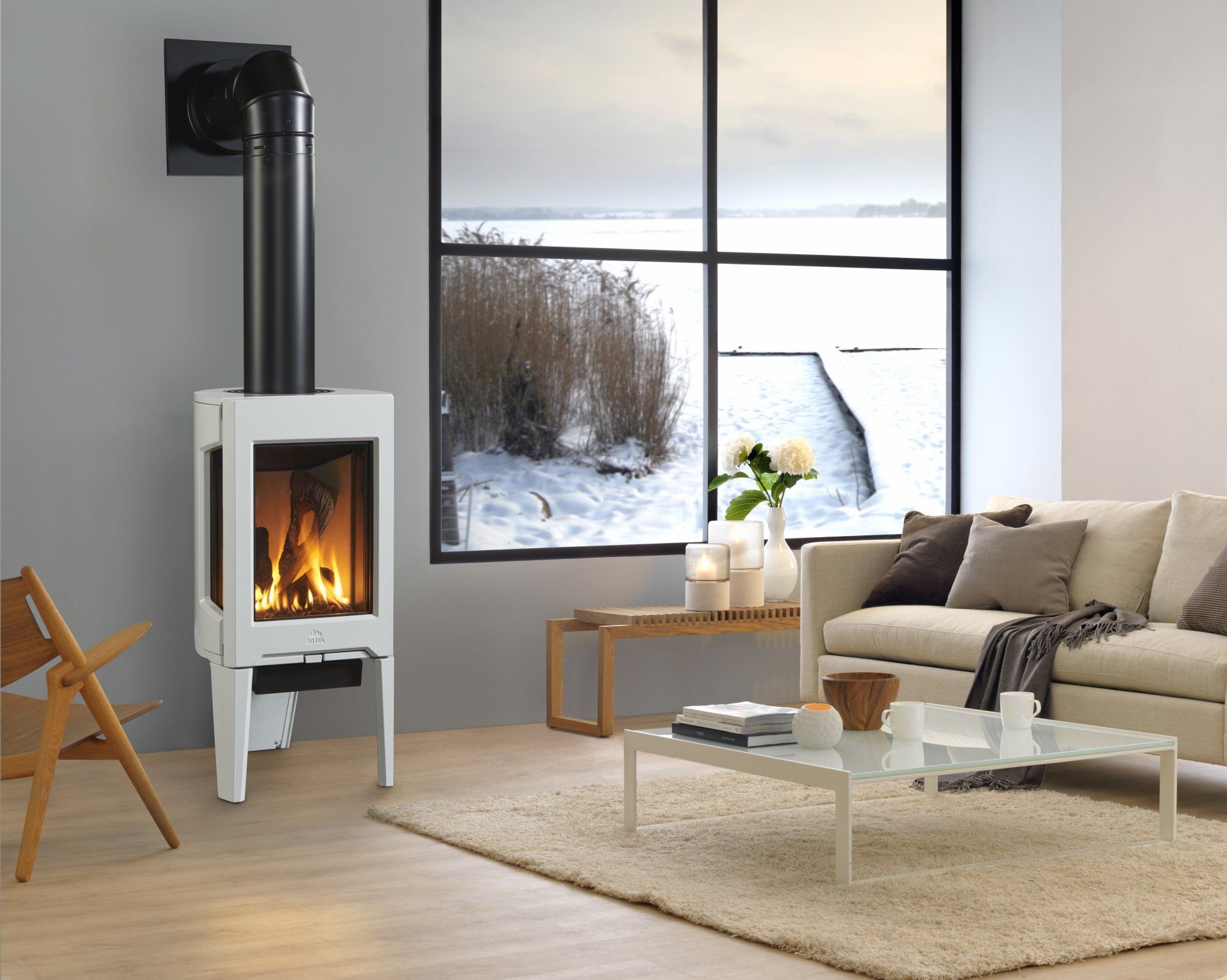 White stove with black chimney in a living room, snowy landscape visible through a window.