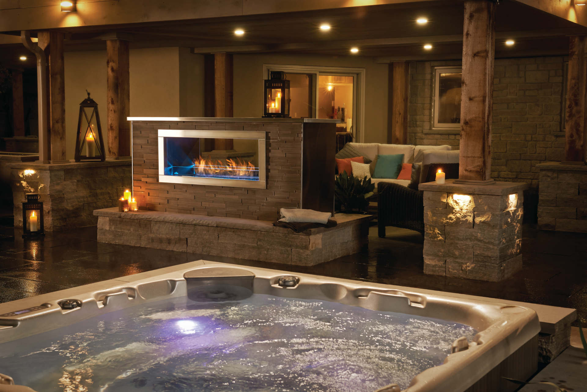 Outdoor spa area with hot tub, fireplace, seating, lanterns, and ambient lighting.