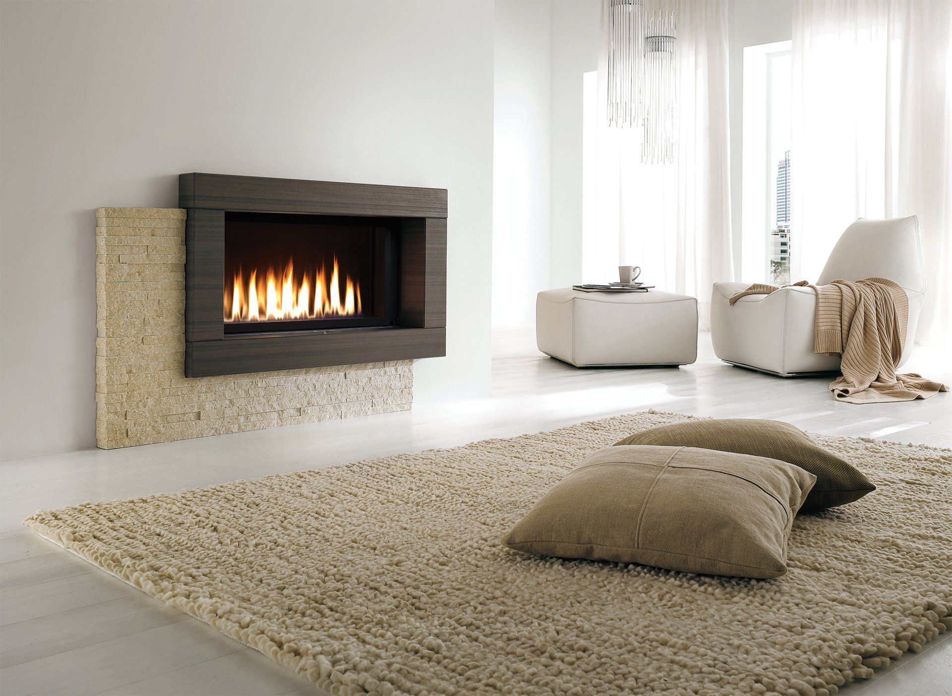 Modern fireplace with flames in a white room; beige rug and pillows, a chair, and a coffee table.