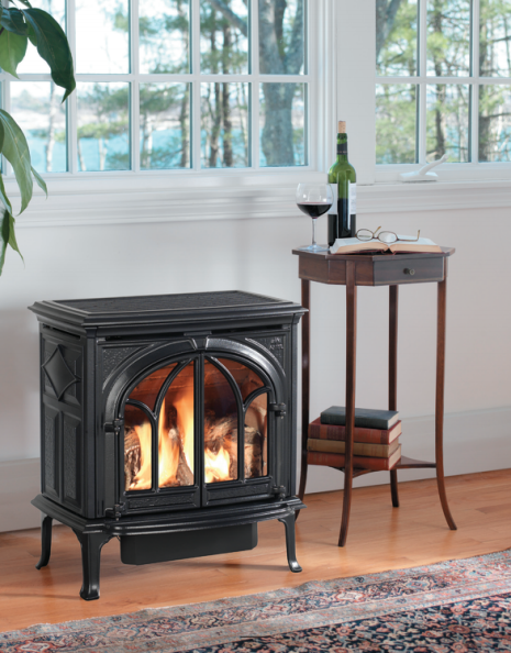 Black stove with fire burning in front of a window, side table with wine, a glass, and a book.