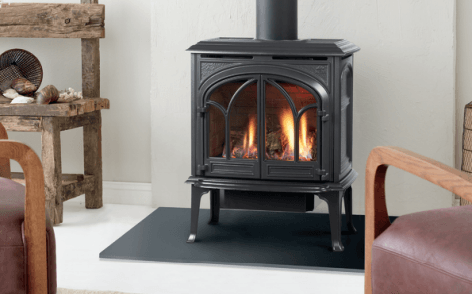 Black gas stove with glowing flames, in a white room, near chairs.