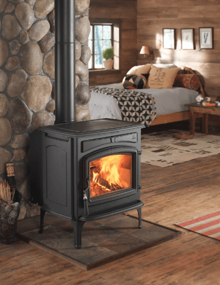 Wood-burning stove in a rustic room with a fire; bedroom in the background.