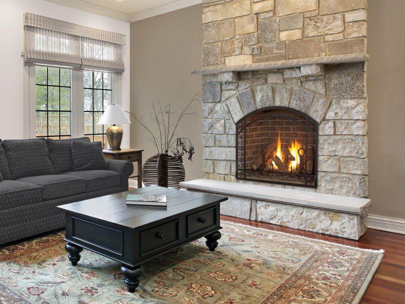 Living room with stone fireplace and burning fire, sofa, coffee table, and area rug.