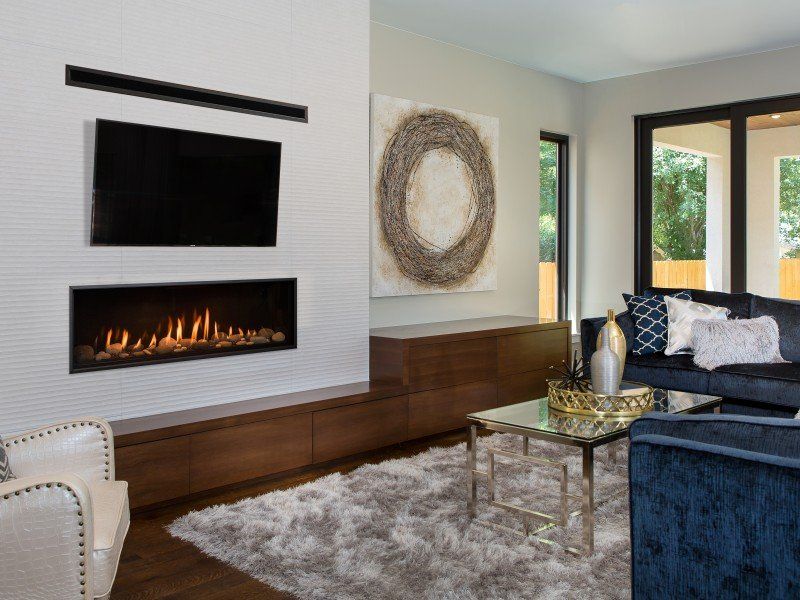 Modern living room with a built-in fireplace and TV on a white textured wall, dark wood cabinets, and a blue sofa.