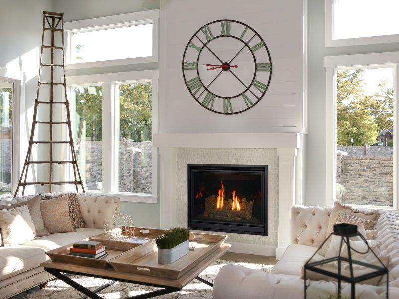 Living room with fireplace, large clock, sofas, windows, and decorative ladder.