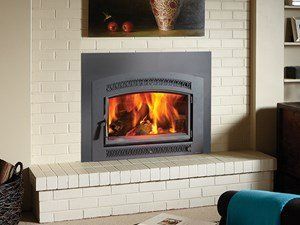 A fireplace with burning logs set in a brick hearth and wall, under a painting.