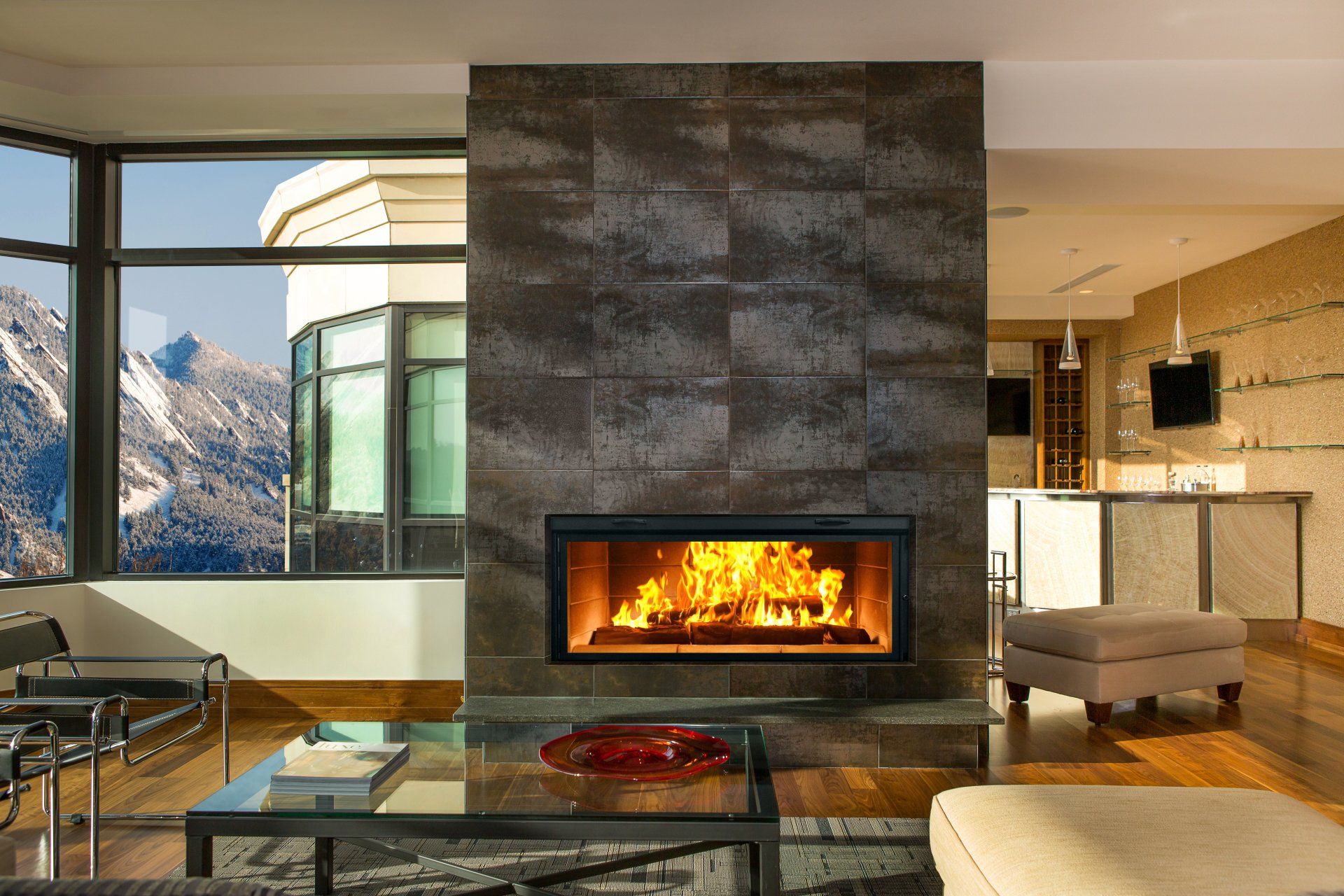 Modern fireplace with flames, gray tile surround, and mountain view through a window.