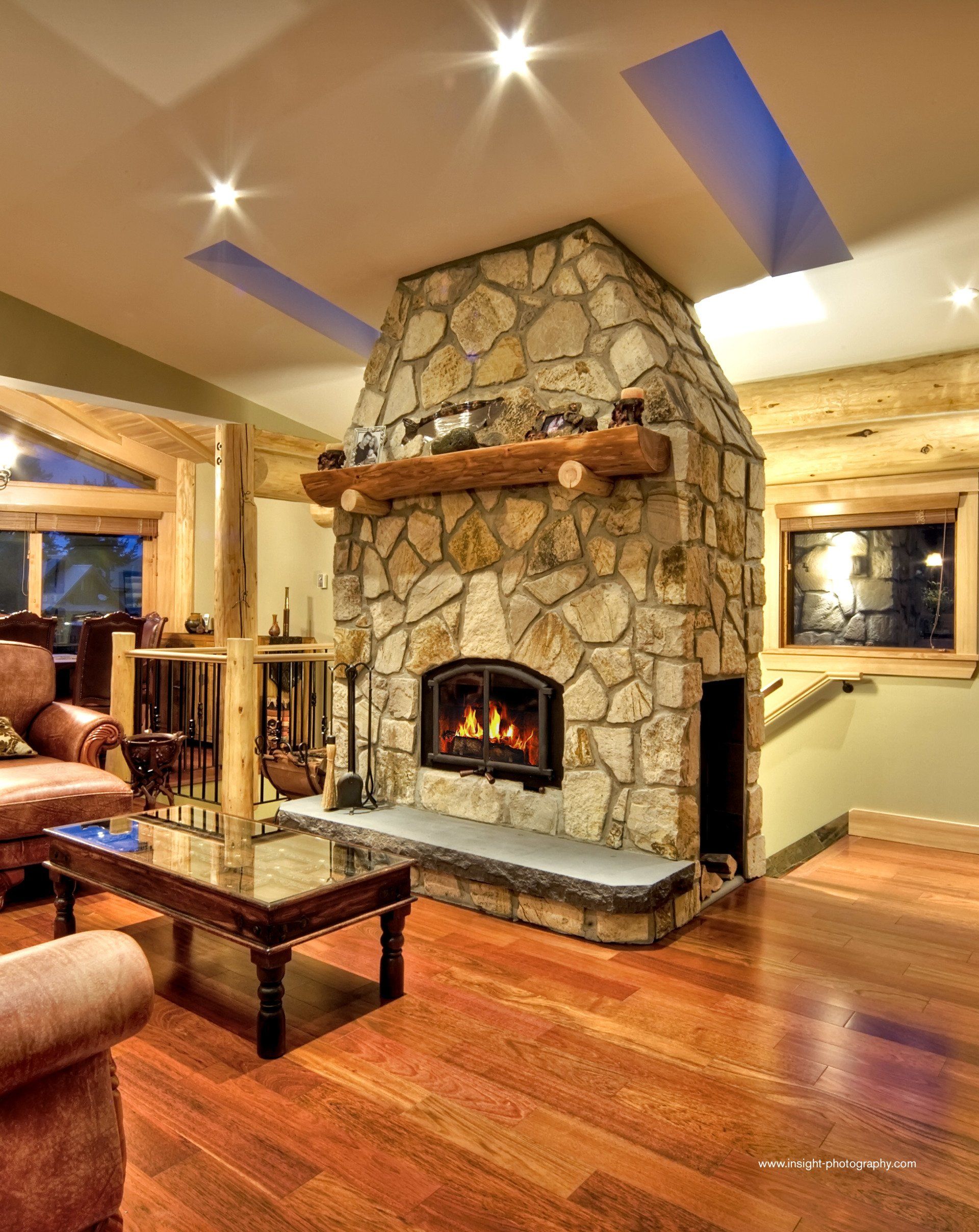 Stone fireplace in a living room with wooden floors and ceiling beams.