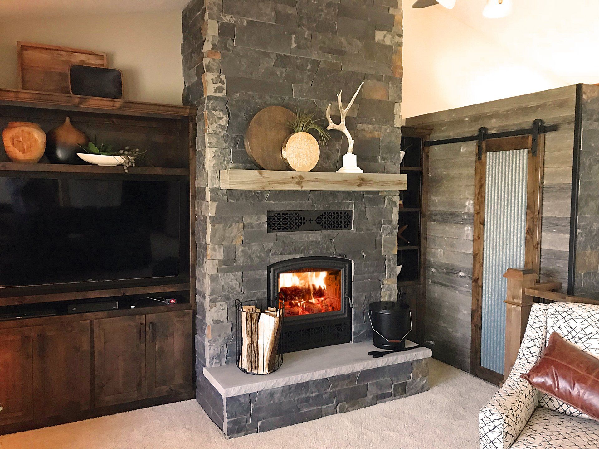 Fireplace in a room with a stacked stone facade, wood mantel, and a burning fire.