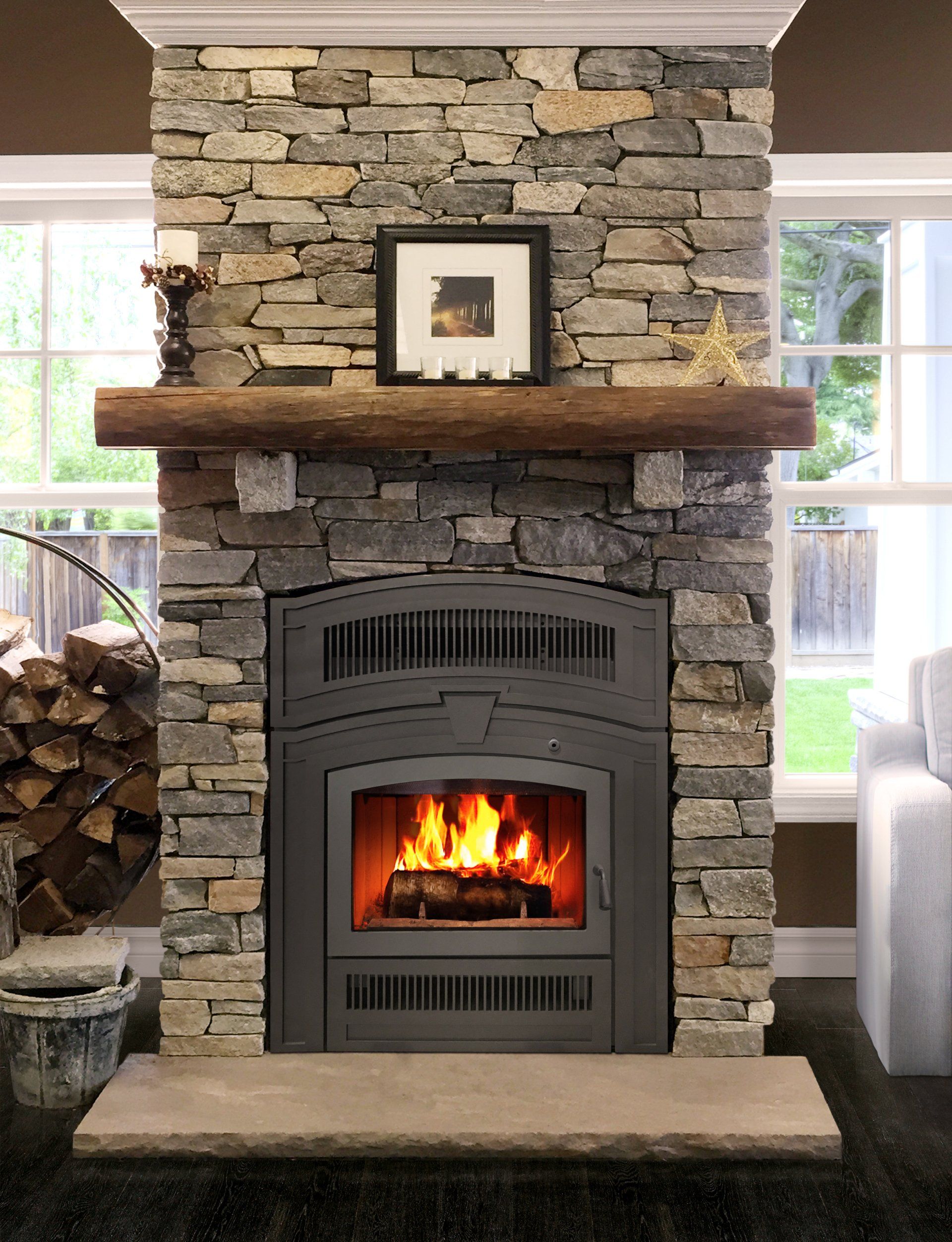 Stone fireplace with burning fire and wooden mantel, flanked by windows.