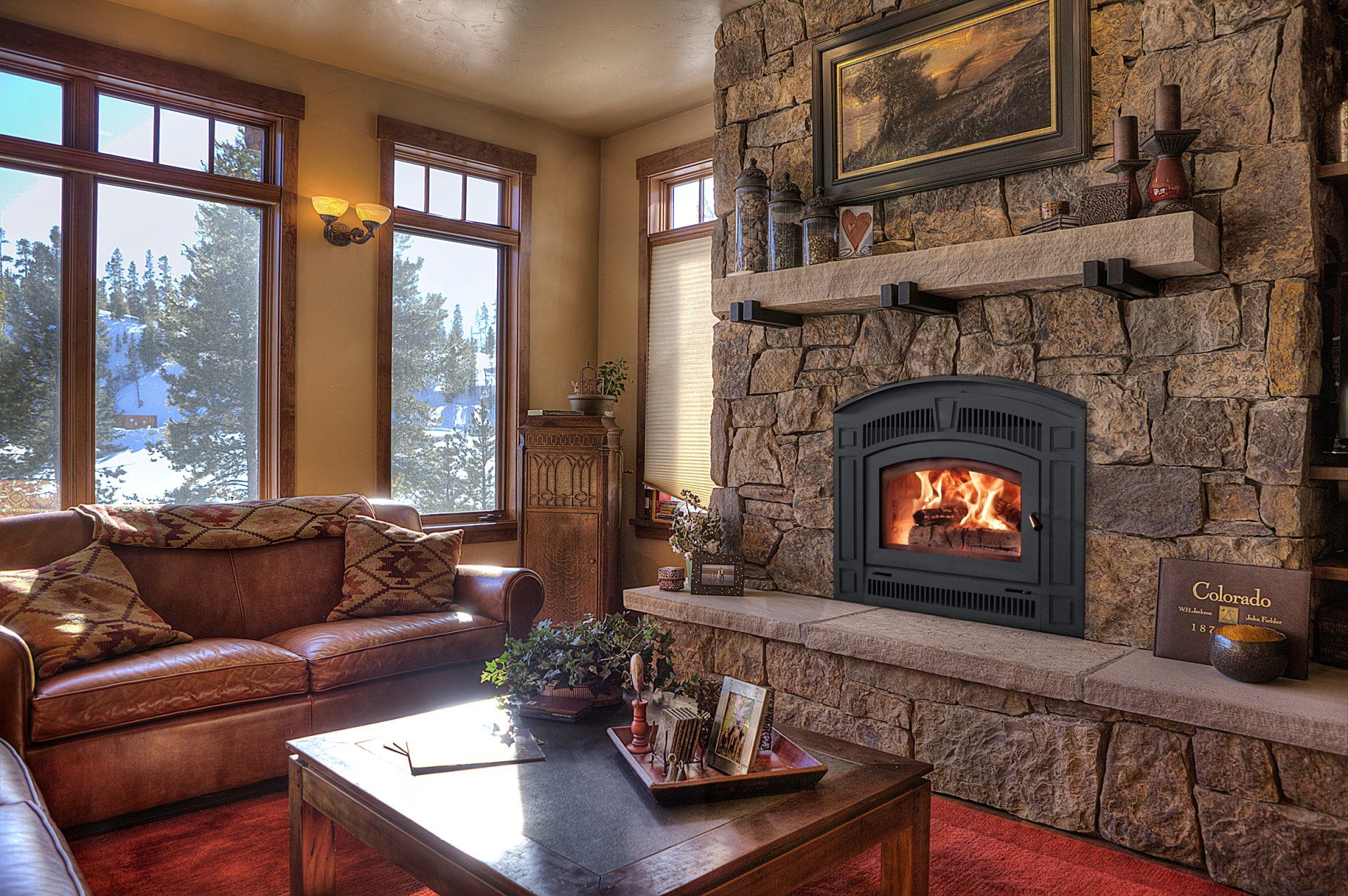 Cozy living room with stone fireplace, burning fire, brown sofa, and windows with snowy view.