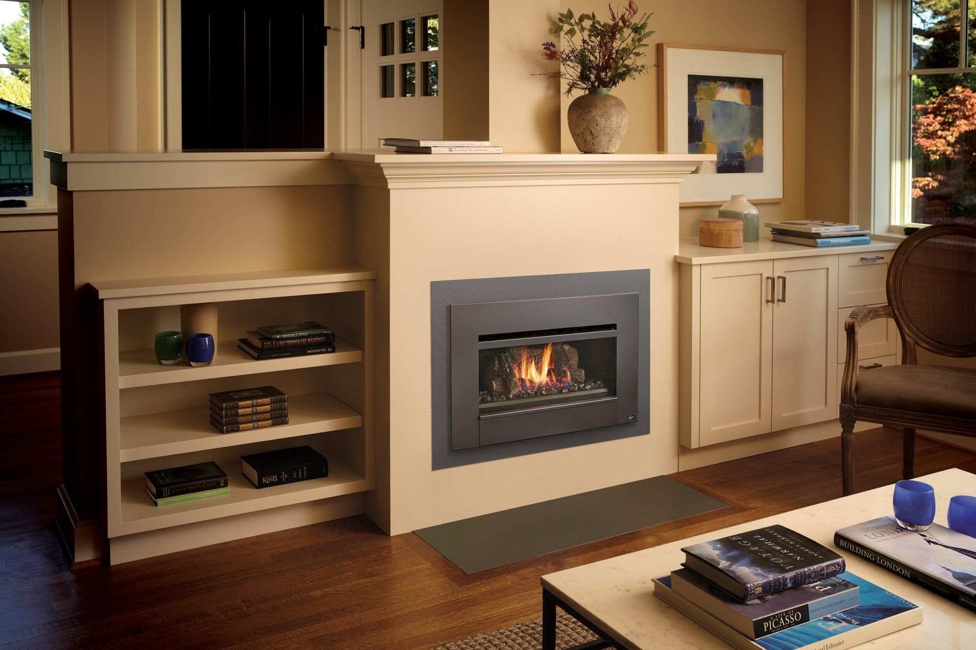 Fireplace built into a wall with shelving and cabinets. Beige and wood tones. Fire is lit.