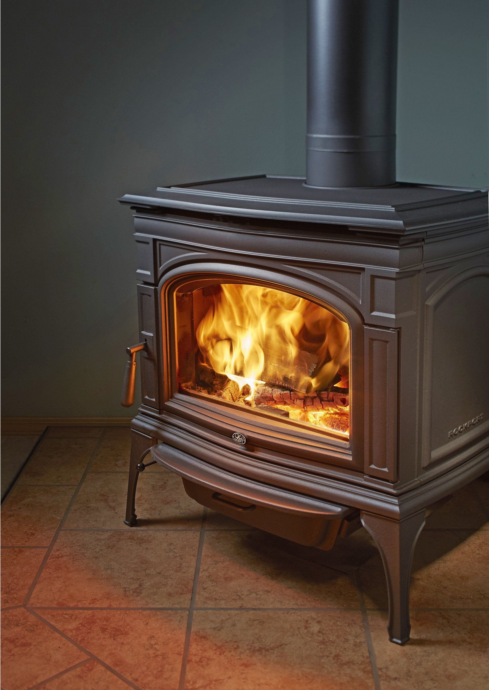 Wood-burning stove with flames visible inside, black metal exterior, set against a dark wall and tiled floor.