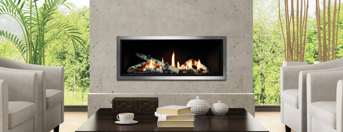Living room with lit fireplace set into a textured stone wall, with greenery visible through the windows.