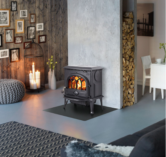 Cozy living room with a black cast iron stove, candles, and framed photos on a wooden wall.