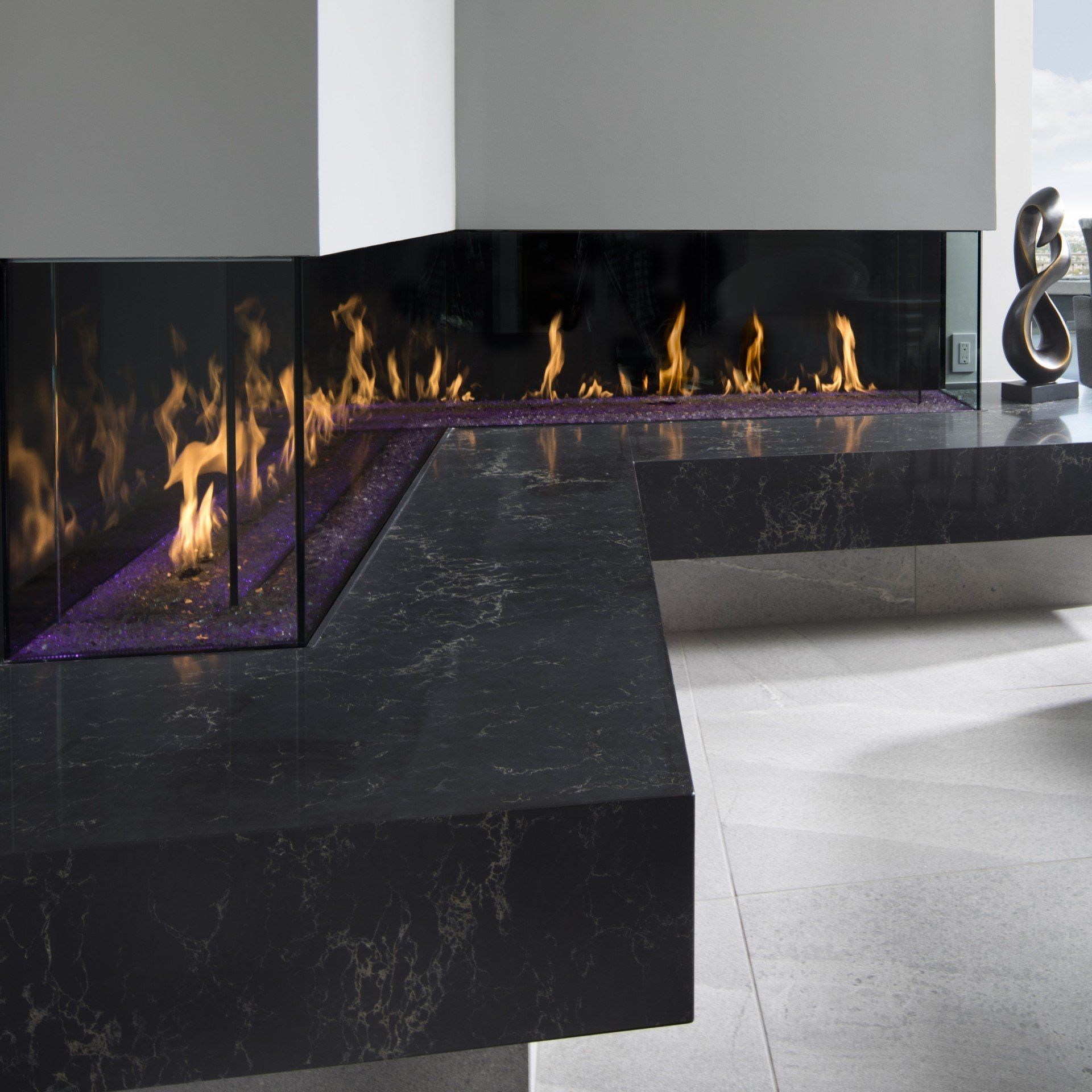 Modern fireplace with black marble surround, glass firebox, and flickering orange flames.