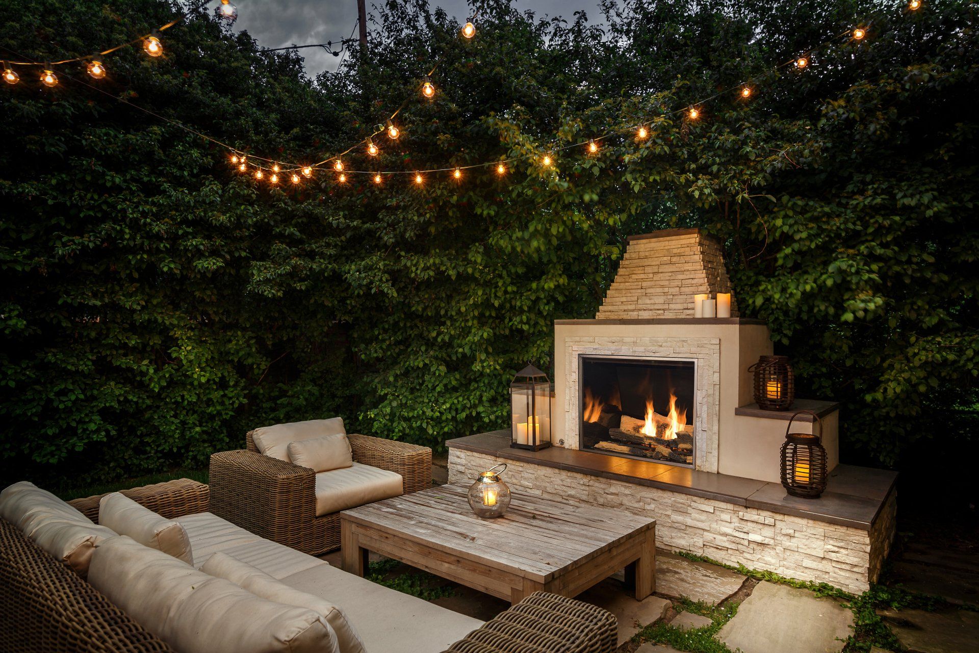 Outdoor fireplace and seating area at night with string lights.