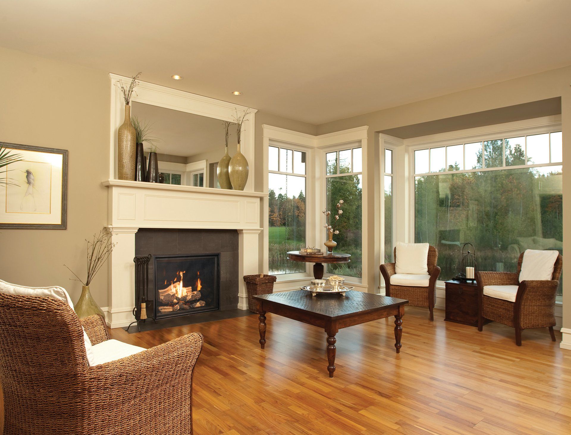 Living room with fireplace, bay window, wicker chairs, hardwood floor.