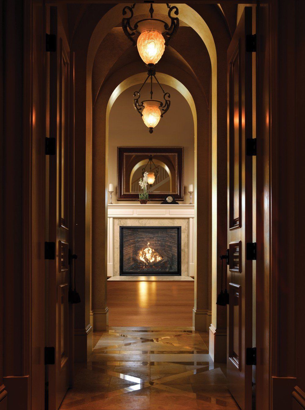 Hallway with arched doorways, ornate light fixtures, fireplace at the end. Warm lighting, wooden floors.