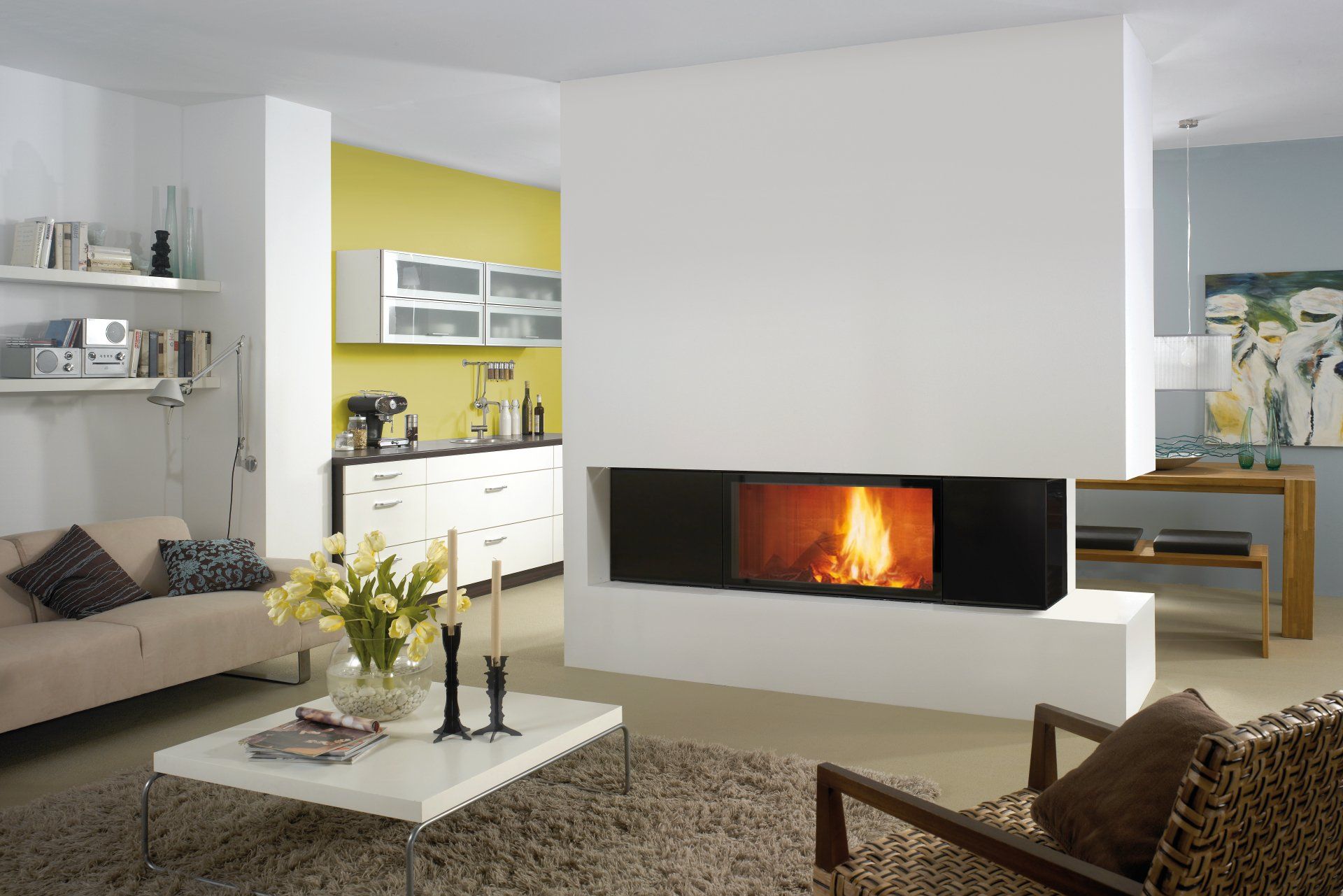 Living room with fireplace, open to kitchen. White walls, beige sofa, modern furniture, and a bright yellow accent wall.