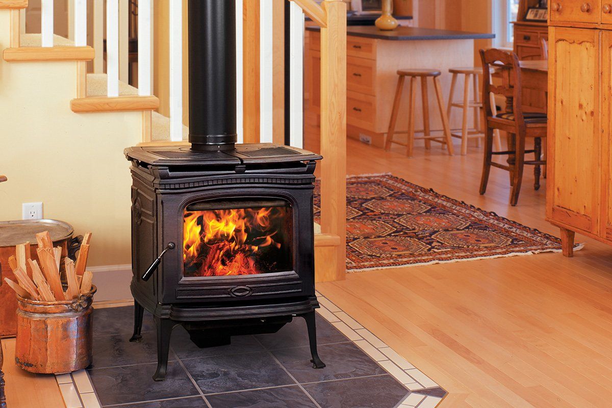 Wood-burning stove with flames, in a home with wooden floors, stairs, and a rug.