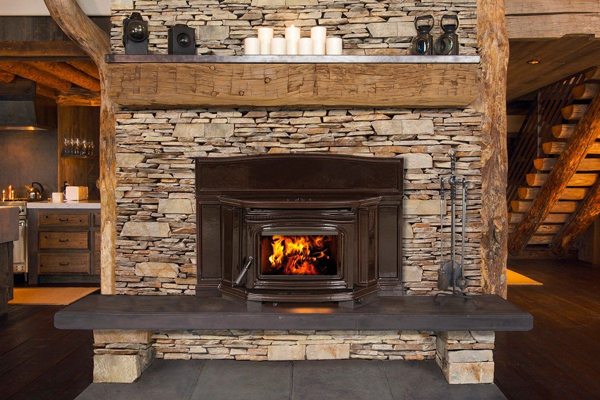 Stone fireplace with burning fire and wood mantel, surrounded by stone and beams.