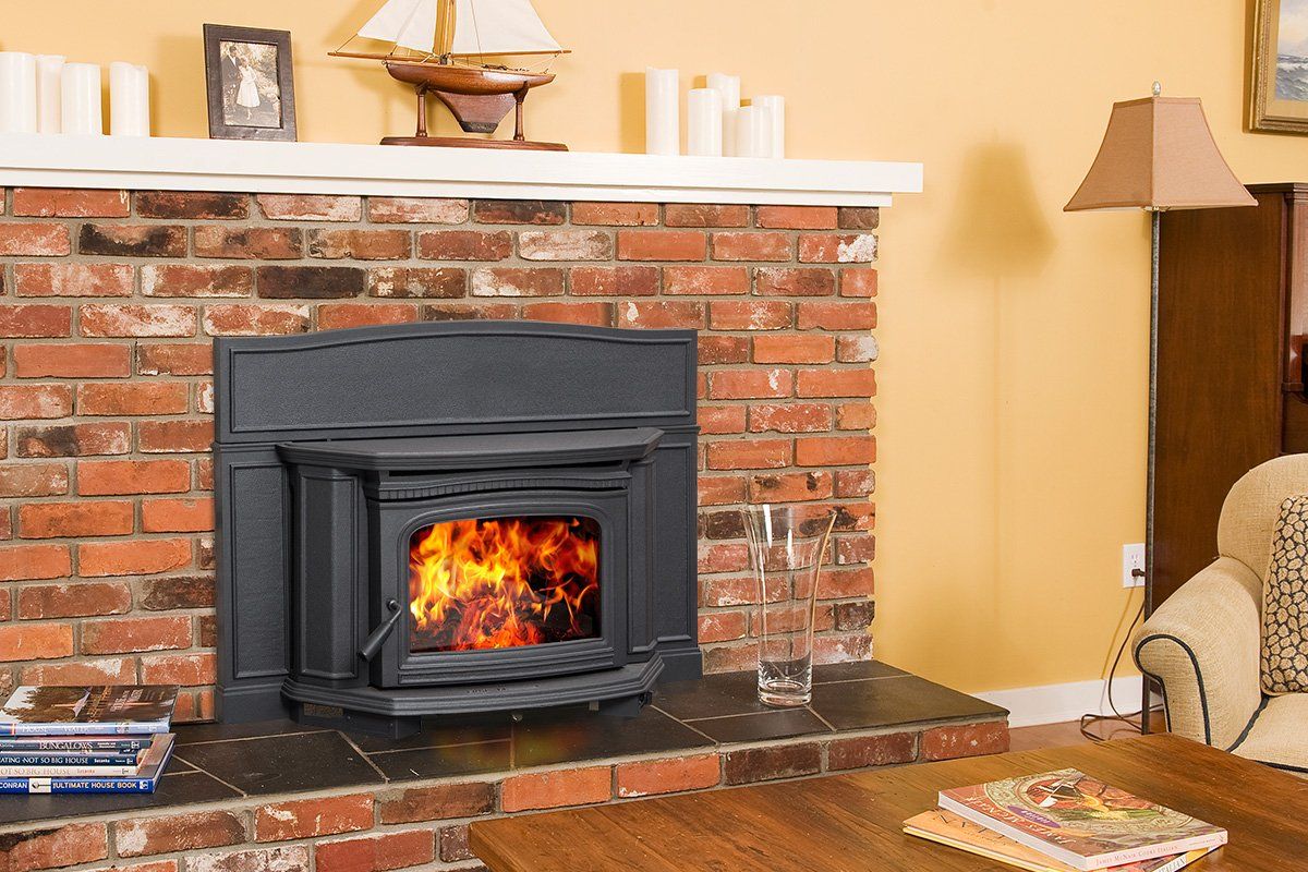 Fireplace with flames in a brick surround, white mantel with candles, model boat, and books, in a cozy living room.