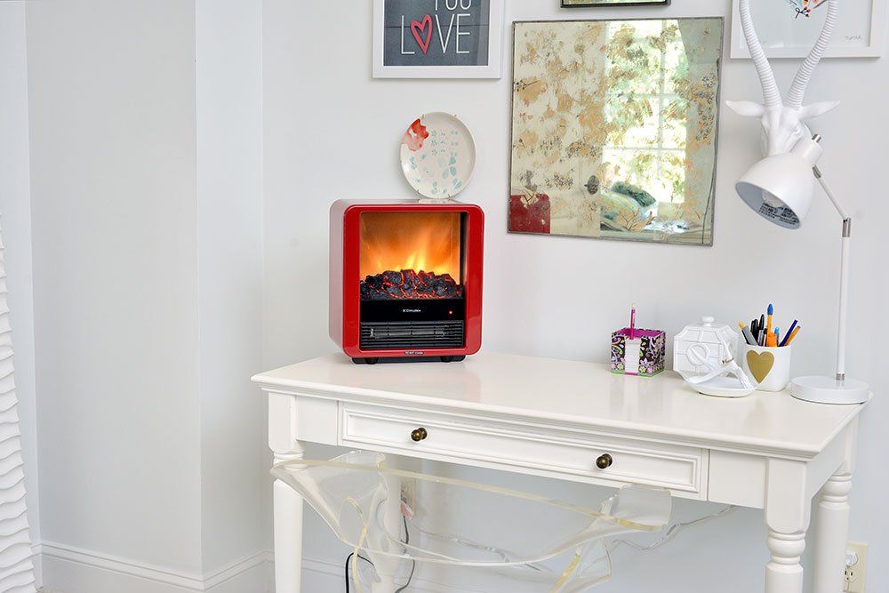 Red electric fireplace on a white desk with decorative items in a room.