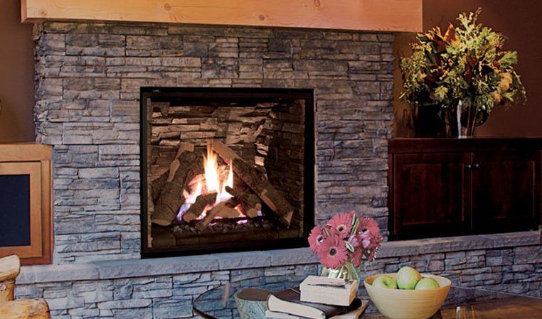 Fireplace with stone surround, lit fire, wooden mantel, flowers, and a cabinet.
