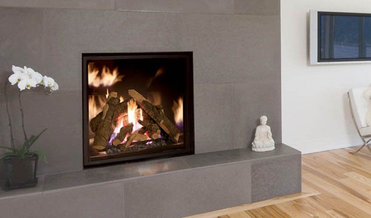 Fireplace with burning logs, built into a gray tiled wall, with a white orchid and a Buddha statue nearby.