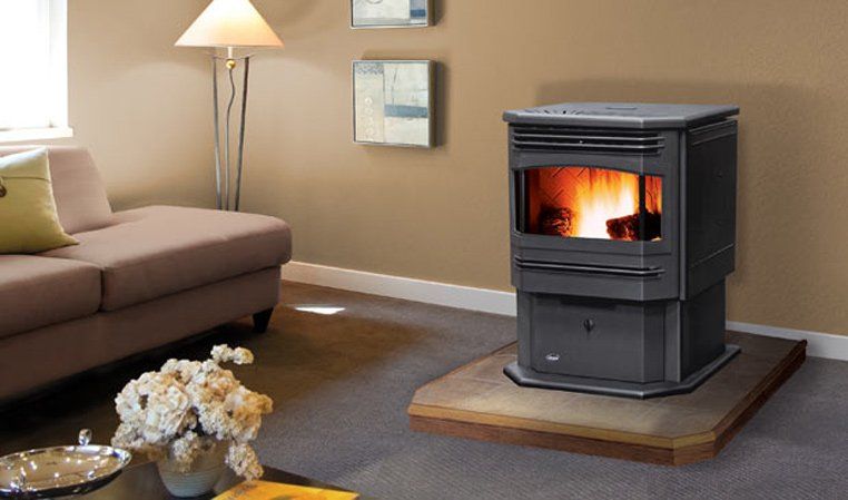 A dark pellet stove with flames burning in a living room, near a couch and lamp.