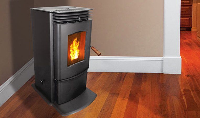 Black pellet stove with flames, set on a hardwood floor against a tan wall with white trim.