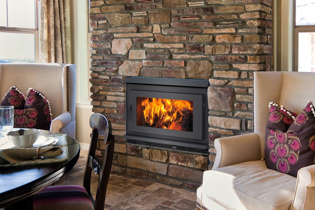 Fireplace with burning flames set into a stone wall, flanked by chairs and a dining table.