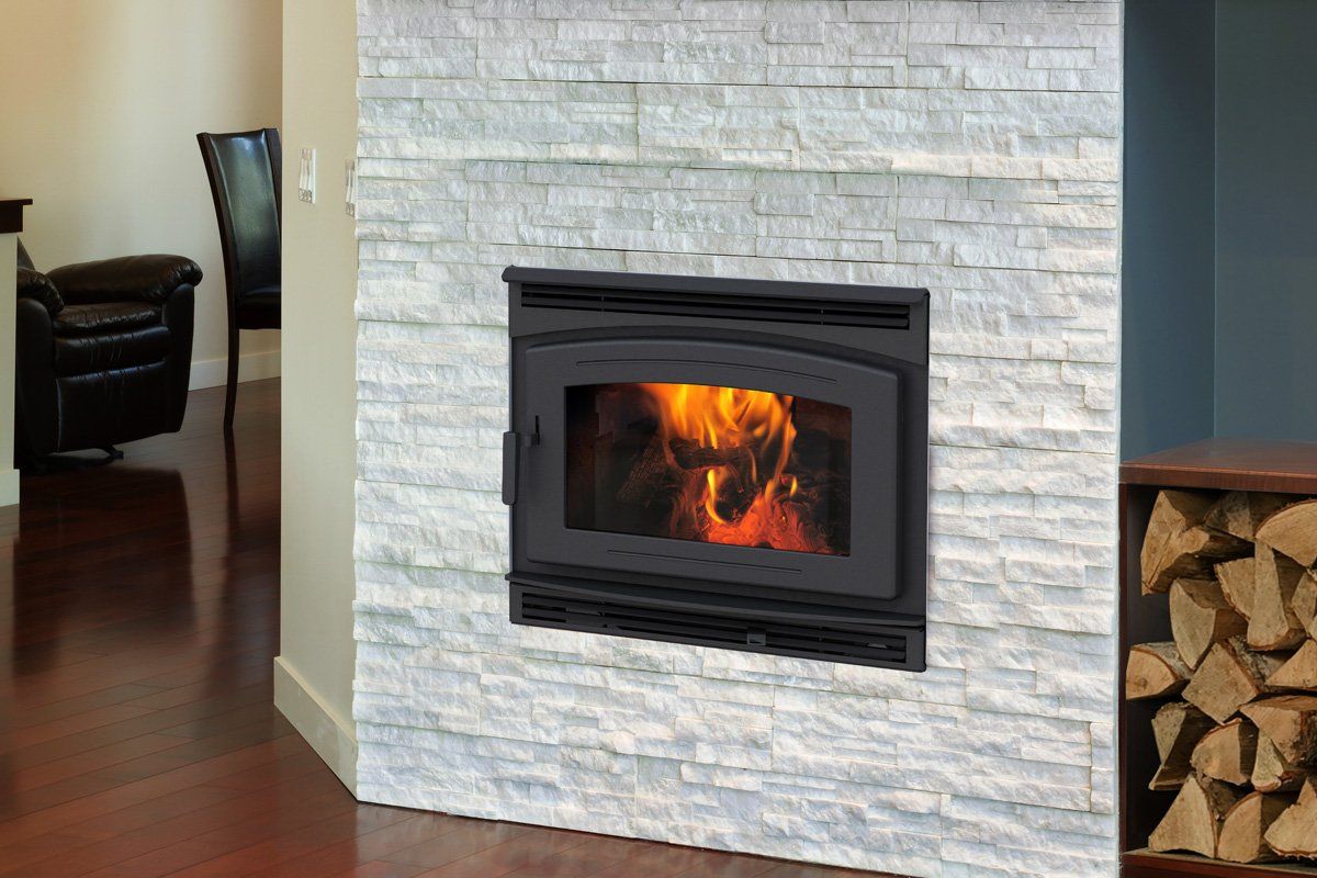 Fireplace with flames in a white stone wall, wooden floor, chair visible.
