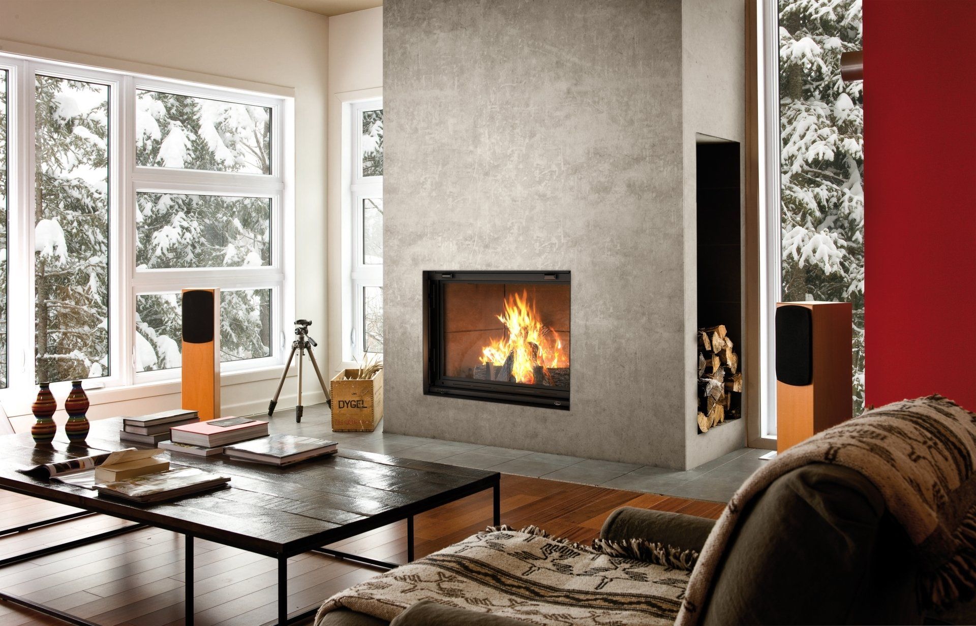 Cozy living room with fireplace, speakers, snow outside windows, black coffee table, and a patterned blanket.