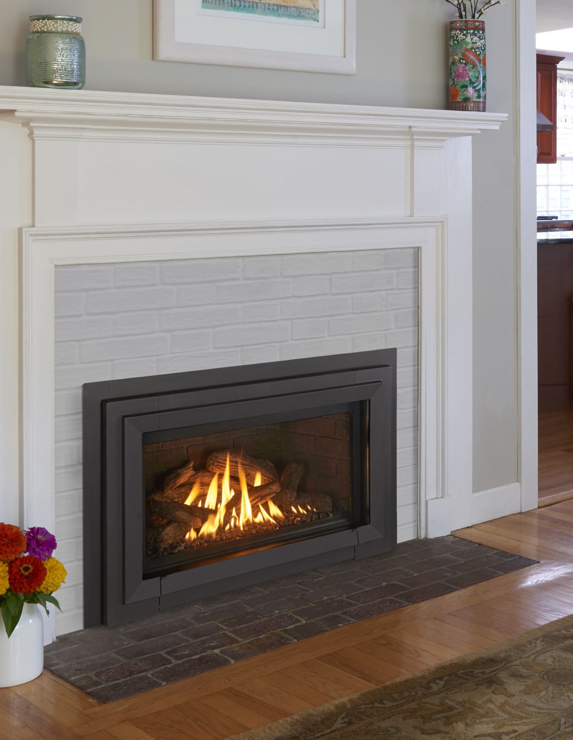 Fireplace with a lit fire, surrounded by a white mantel and grey brick.