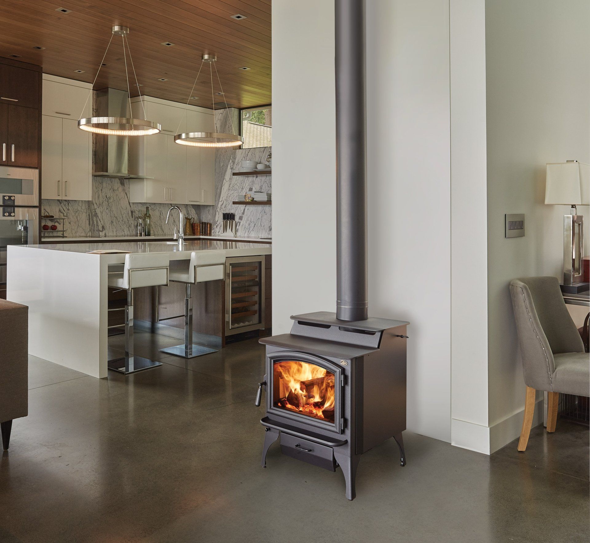 Wood-burning stove in modern home. Open flame visible; kitchen and living areas in background.