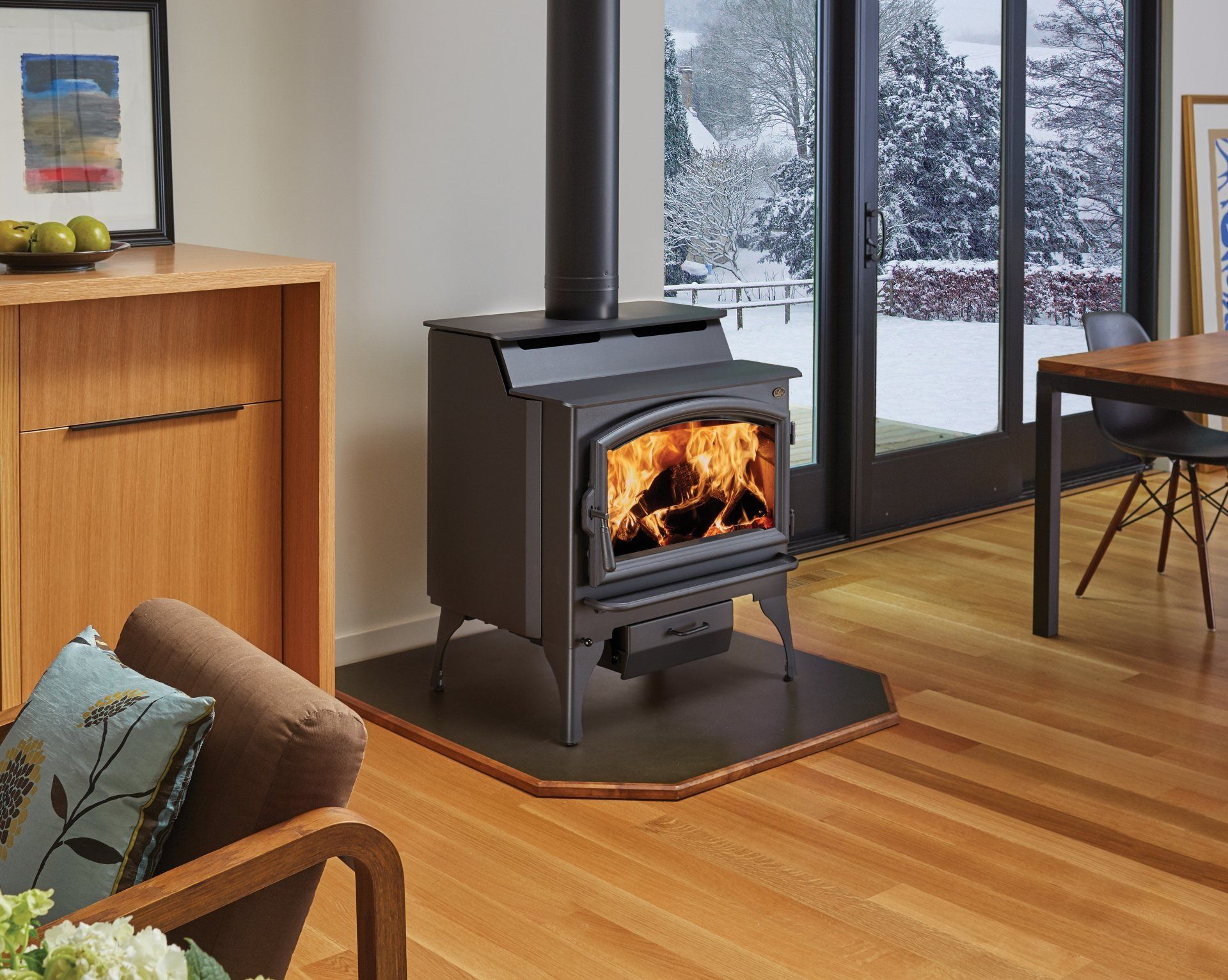 Wood-burning stove with flames in a cozy living room, snowy outdoor view.
