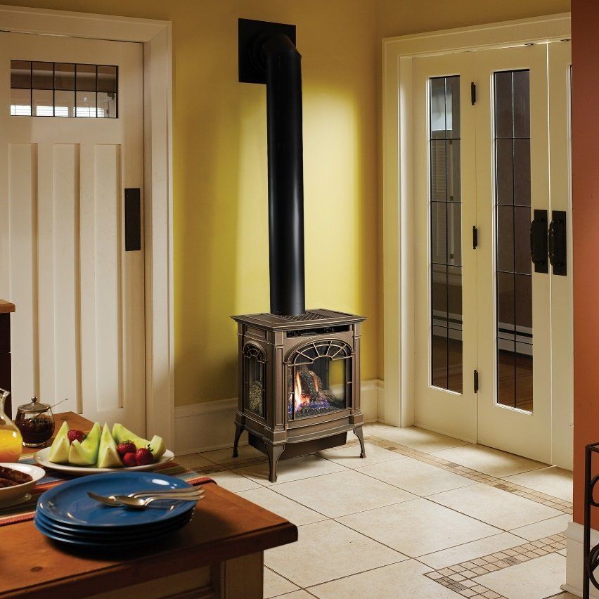 Fireplace in a kitchen with a black chimney and glass doors. Yellow walls and tile flooring.