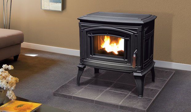 Black cast iron pellet stove burning, set on tiled hearth in a room with neutral walls.