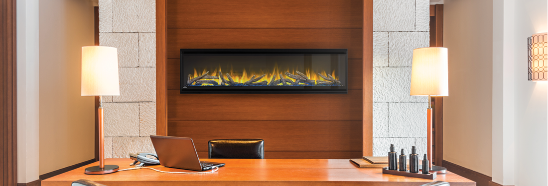 A modern office desk with a fireplace and lamps. The desk is brown, with a laptop, phone, and decorations.