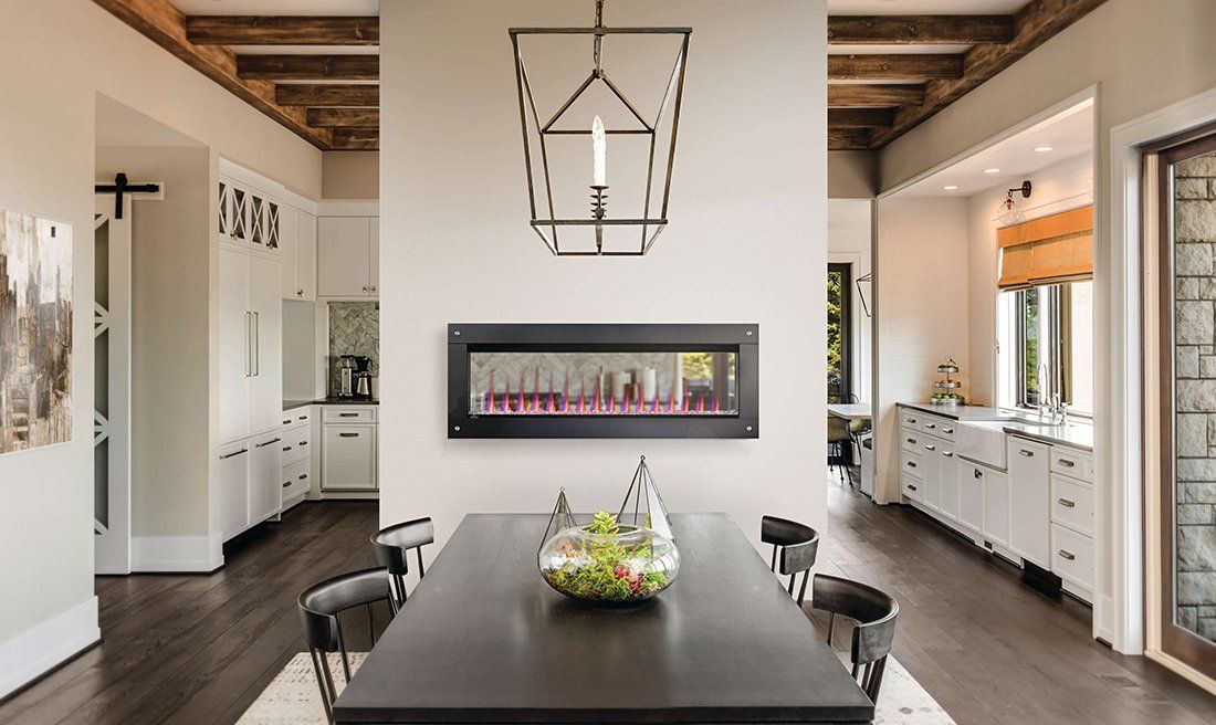Dining room with dark table, modern fireplace, and kitchen visible in the background.
