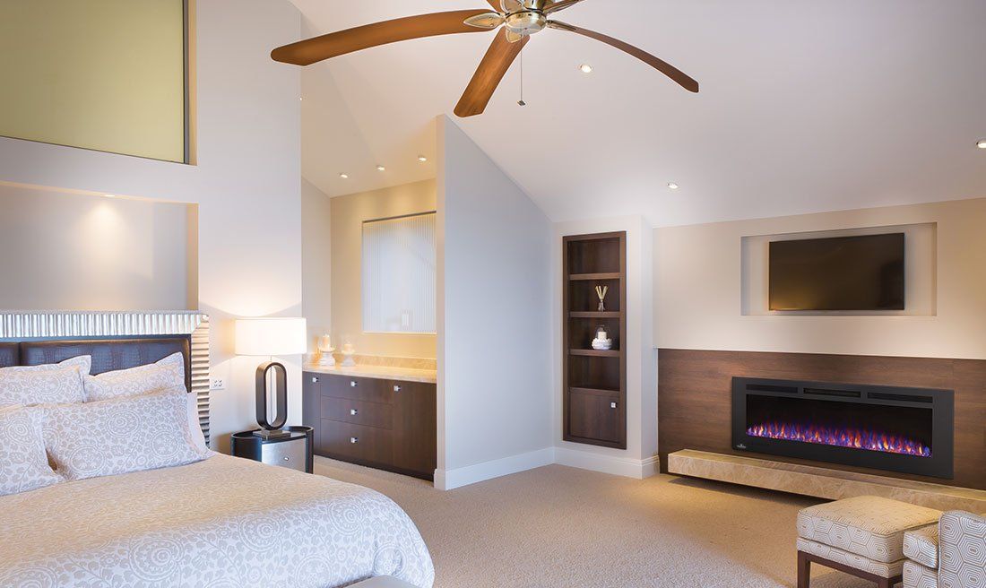 Bedroom with a bed, fireplace, built-in shelving, TV, and ceiling fan. Neutral colors.