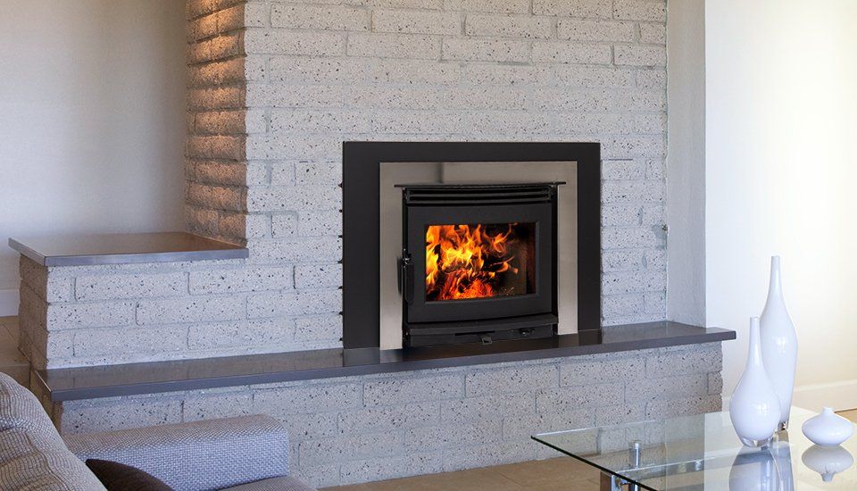 Fireplace with a lit fire, set in a light grey stone wall and surrounded by a dark metal frame.